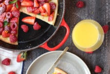 Slice of dutch baby on a plate topped with berries next to a pan.