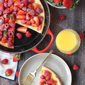 Slice of dutch baby on a plate topped with berries next to a pan.