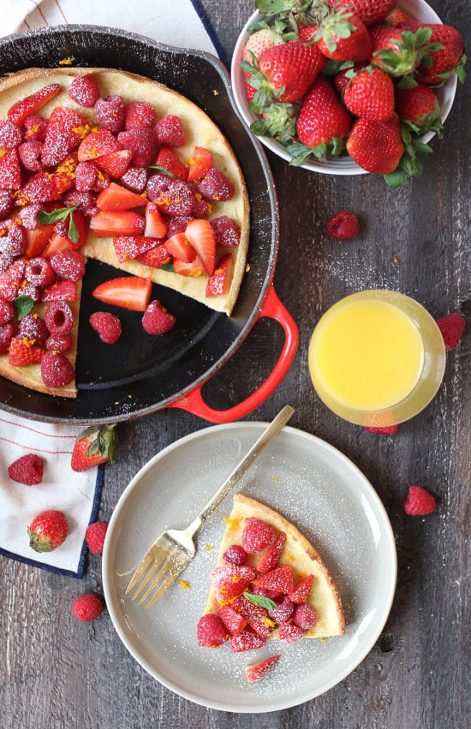 Slice of dutch baby on a plate topped with berries next to a pan. 