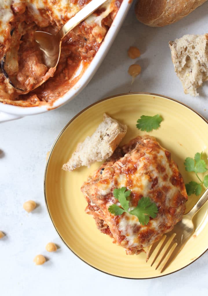 birds eye view of of plant-based moussaka with gluten free hummus "bechamel" sauce served on a yellow plate garnished with fresh herbs