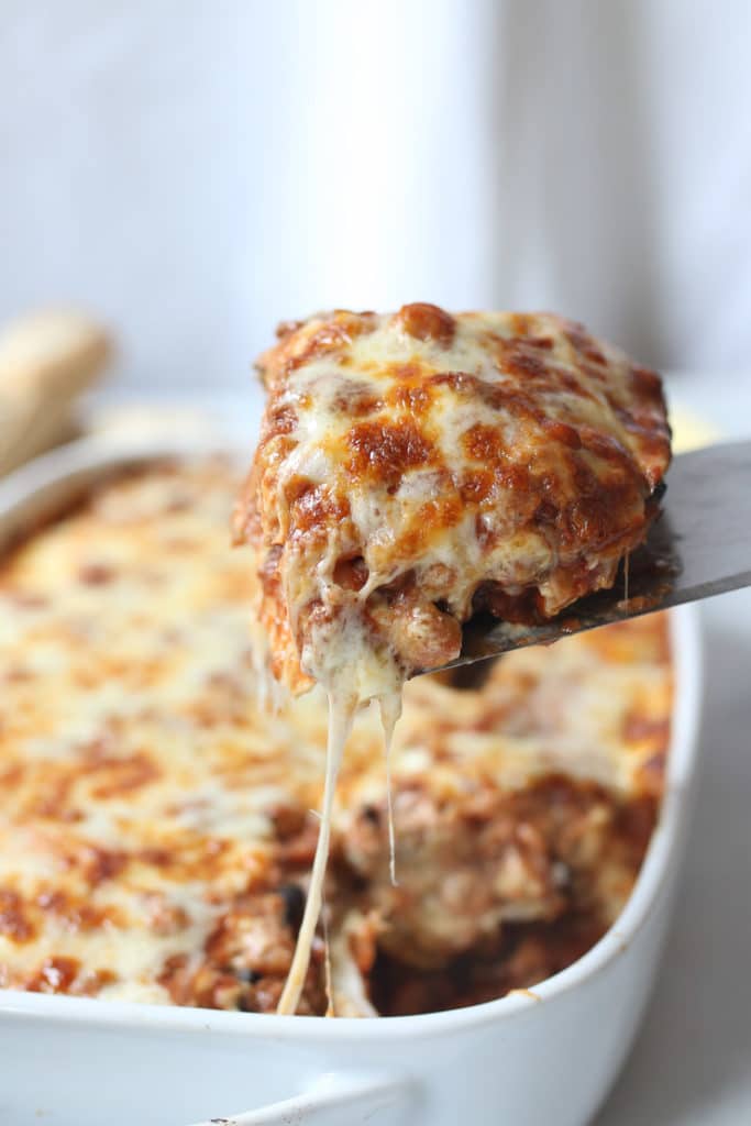 Spatula taking out a serving of cheesy moussaka out of a white casserole dish.