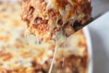 Spatula taking out a serving of cheesy vegan moussaka out of a white casserole dish.