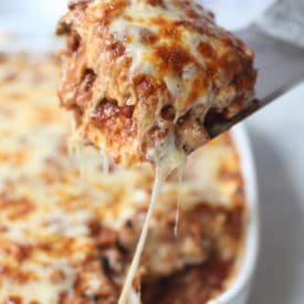 Spatula taking out a serving of cheesy vegan moussaka out of a white casserole dish.