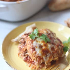 Serving of cheesy vegan moussaka on a yellow plate topped with parsley and a serving of bread.