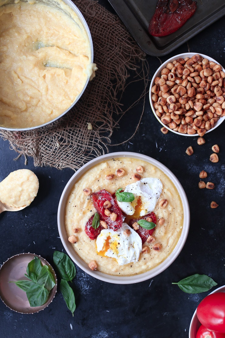 Creamy polenta topped with poached eggs and tomatoes next to a bowl of corn nuts.