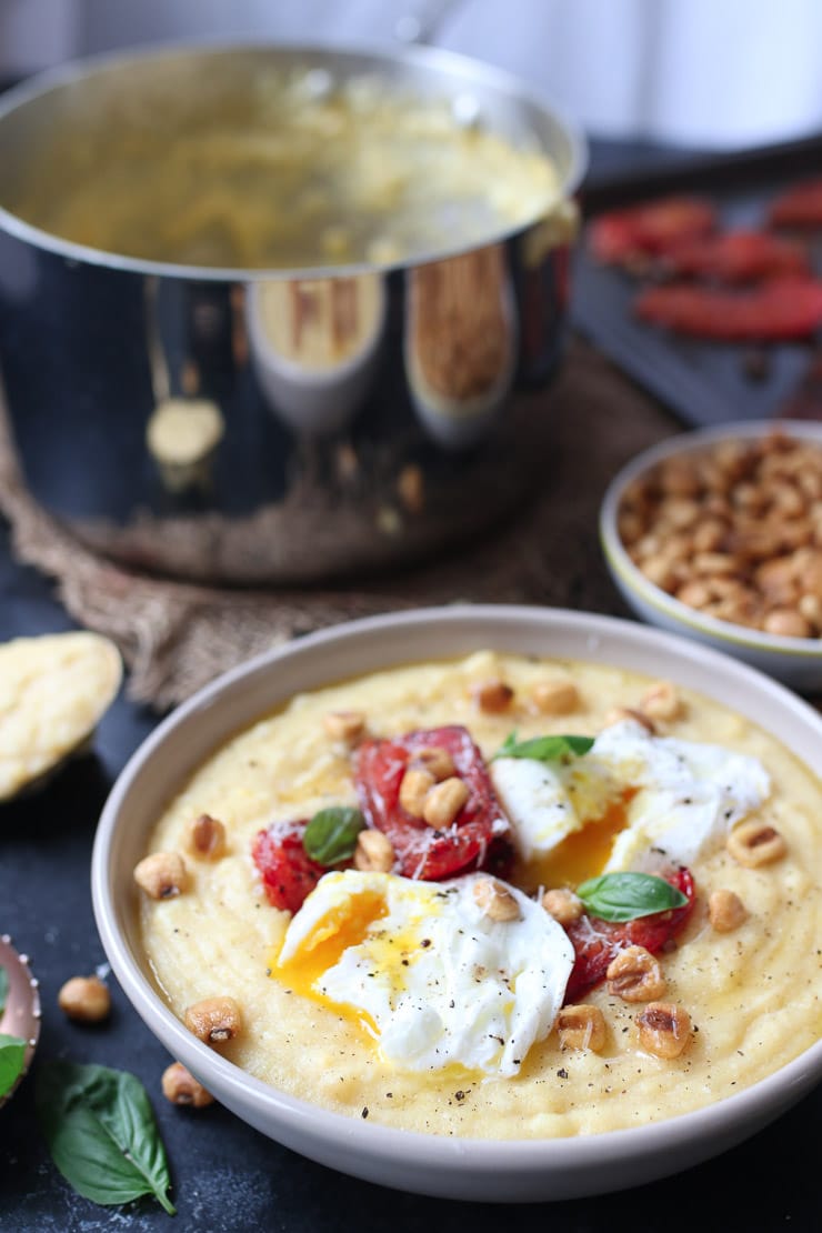Creamy polenta topped with poached eggs and tomatoes next to a bowl of corn nuts.