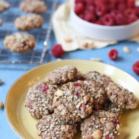 Cookies on a yellow plate next to a bowl of raspberries.