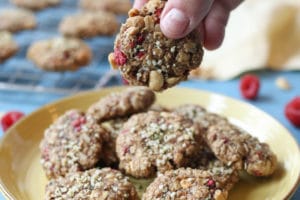 Hand holding a cookie near a yellow plate with cookies.