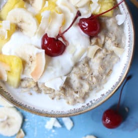 Bowl of oatmeal topped with pineapple, cherries and yogurt.