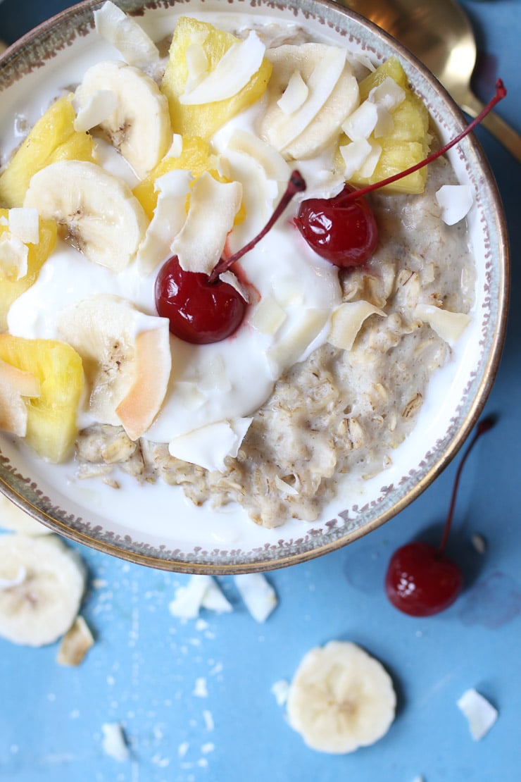 Bowl of pineapple oatmeal topped with pineapple, cherries and yogurt.