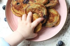 Baby's hand grabbing a baby pancake and a blueberry.