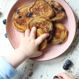 Baby's hand grabbing a baby pancake and a blueberry.