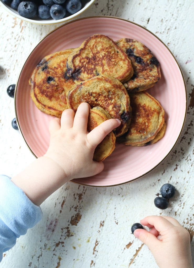 Baby's hand grabbing a baby pancake and a blueberry.