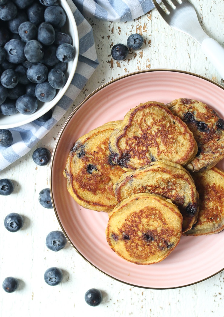 Baby cereal pancakes on a pink plate next to a bowl of blueberries.