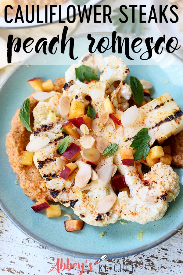 pinterest image of grilled cauliflower steaks with a peach romesco sauce on a teal plate with text overlay