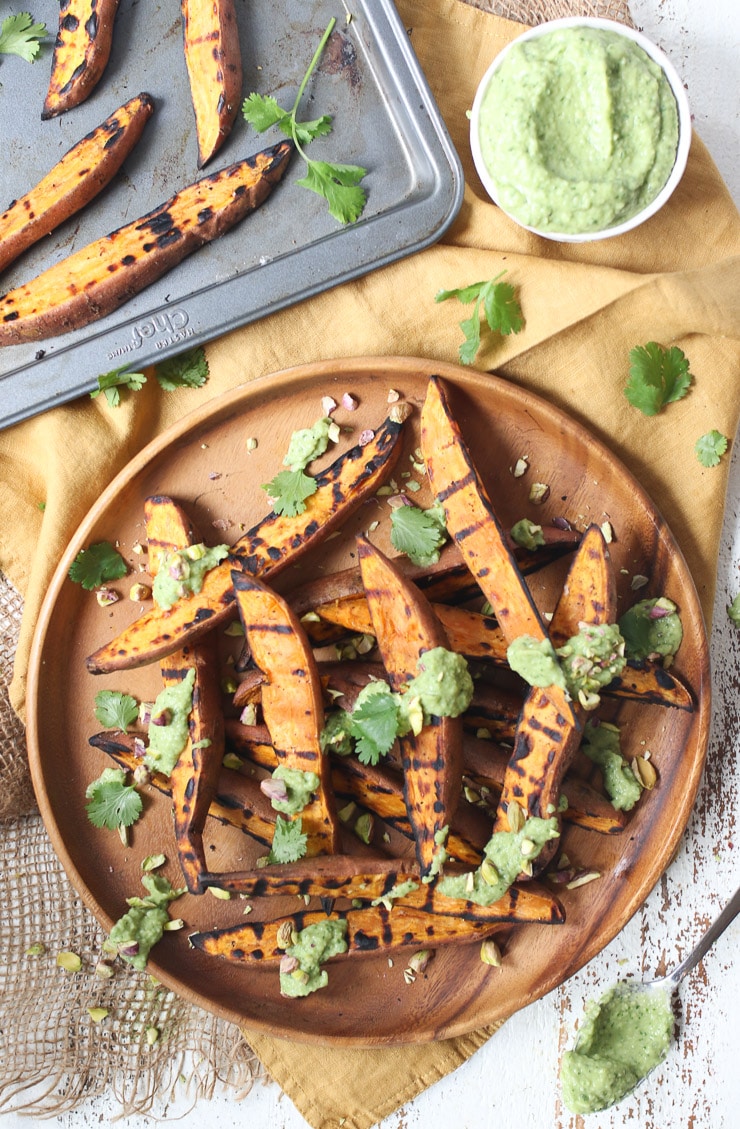 Grilled sweet potato with avocado lime sauce, with a tray of sweet potato wedges in the background.