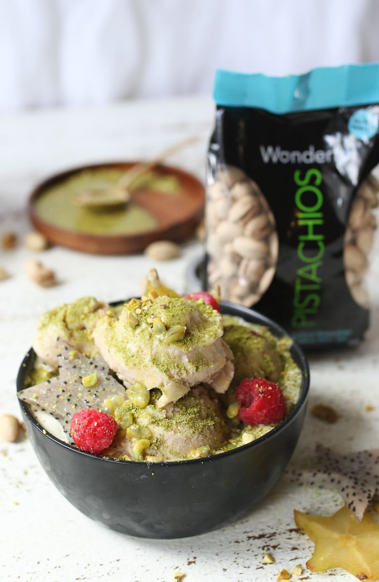 Pistachio green tea nice cream topped with fruit next to a bag of pistachios.