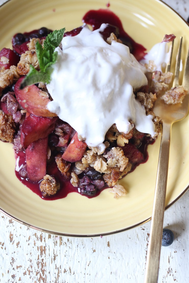 Blueberry and peach crisp on a yellow plate topped with ice cream.