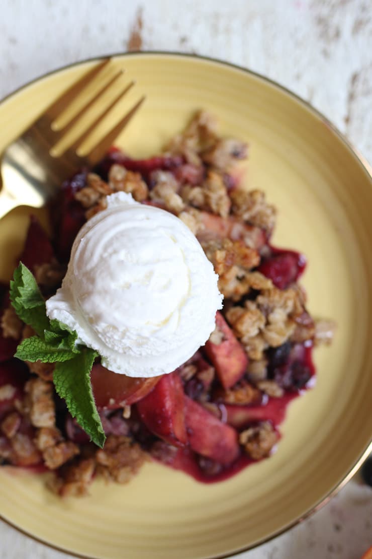 Fruit crisp on a yellow plate topped with ice cream.