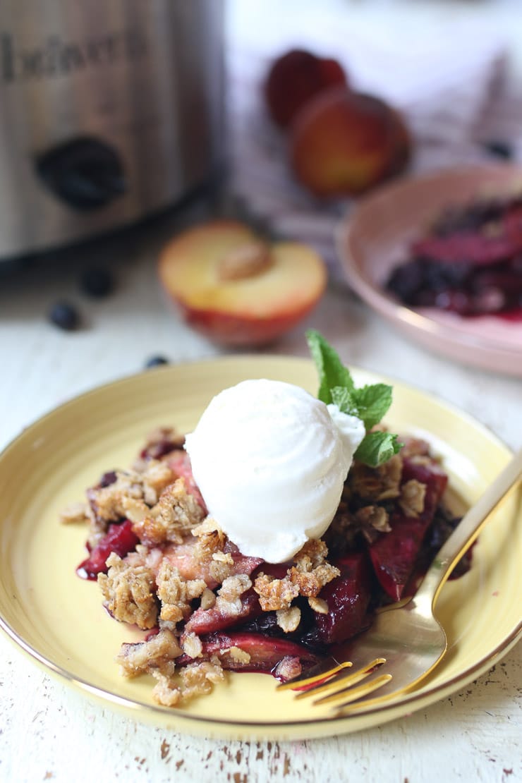 Blueberry and peach crisp on a yellow plate topped with ice cream.