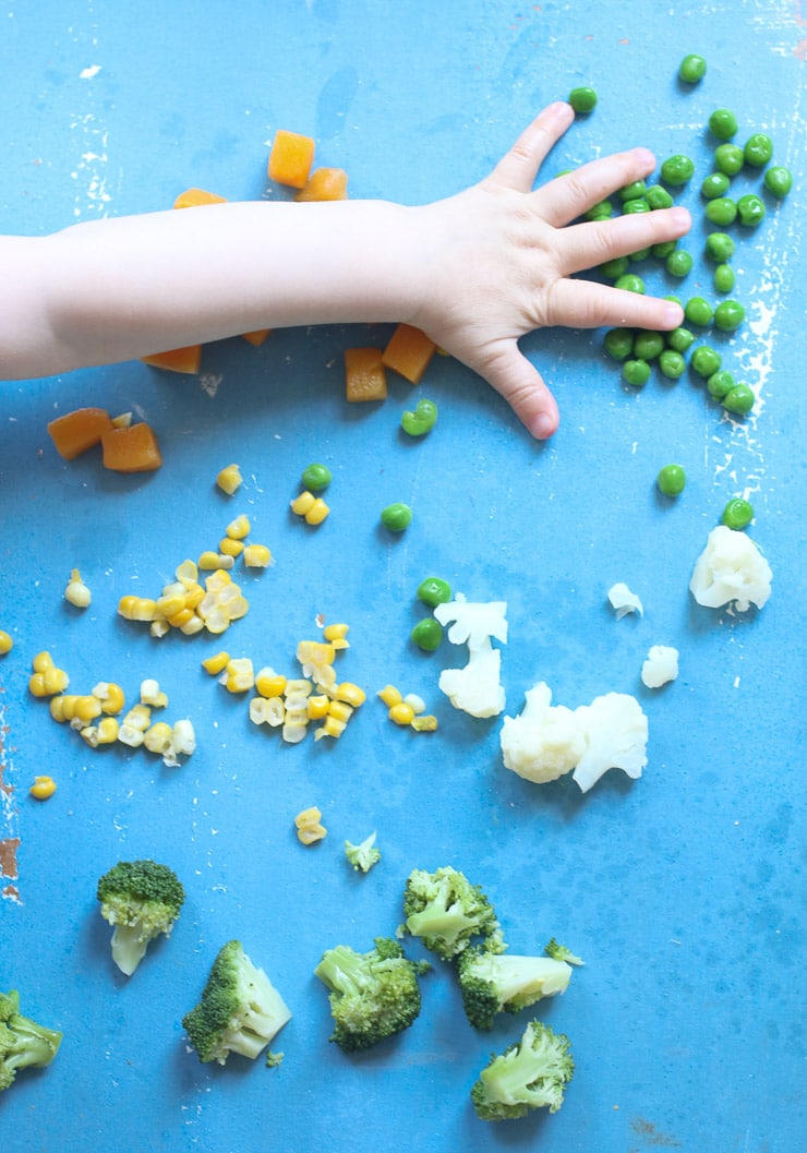 Baby's hand reaching for vegetables to discuss baby led weaning recipes.