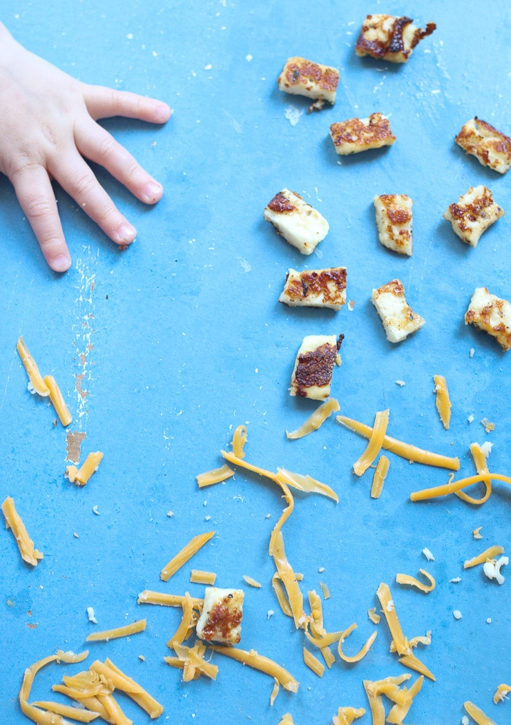Baby's hand reaching for halloumi and cheese to discuss baby led weaning recipes.
