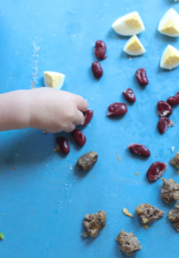 Baby's hand reaching for eggs, kidney beans and meatballs. 