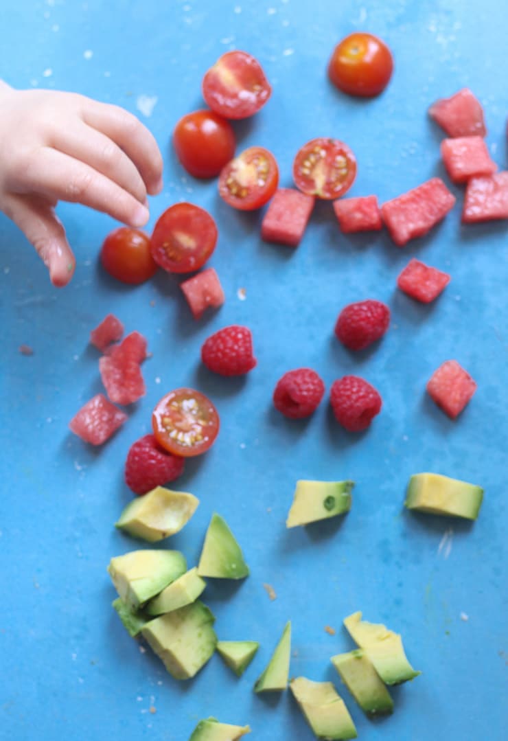 Baby's hand reaching for watermelon and tomatoes.