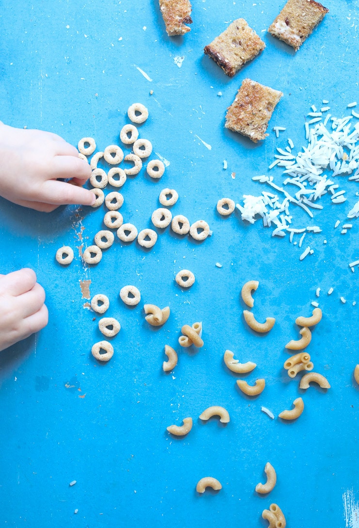 Baby's hand reaching for cereal, macaroni and bread to discuss baby led weaning recipes.