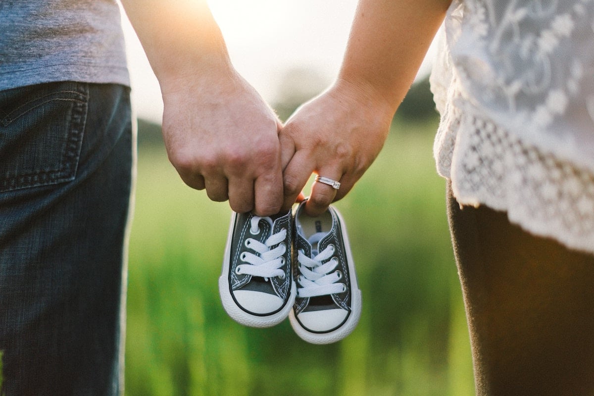 A couple holding one pair of baby shoes.