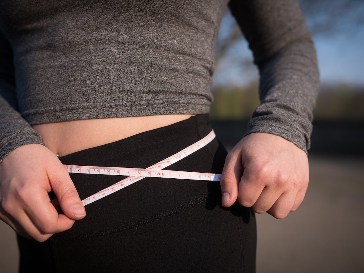 woman measuring her waist line with measuring tape