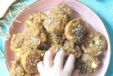 Toddler hand reaching for mini muffins from pink plate.