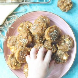 Toddler hand reaching for mini muffins from pink plate.