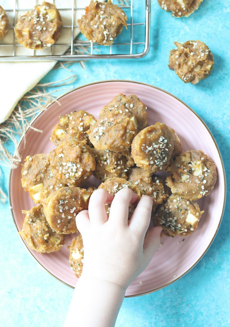 Toddler hand reaching for sweet potato mini muffins from pink plate.