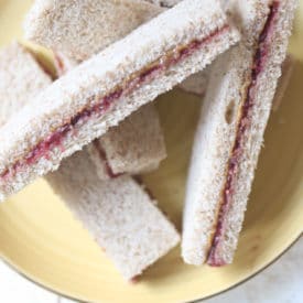 Peanut butter and jelly finger sandwiches on a yellow plate.