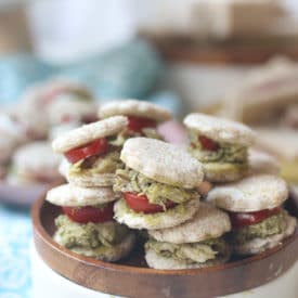 Chicken and pesto finger sandwiches on a wooden plate.