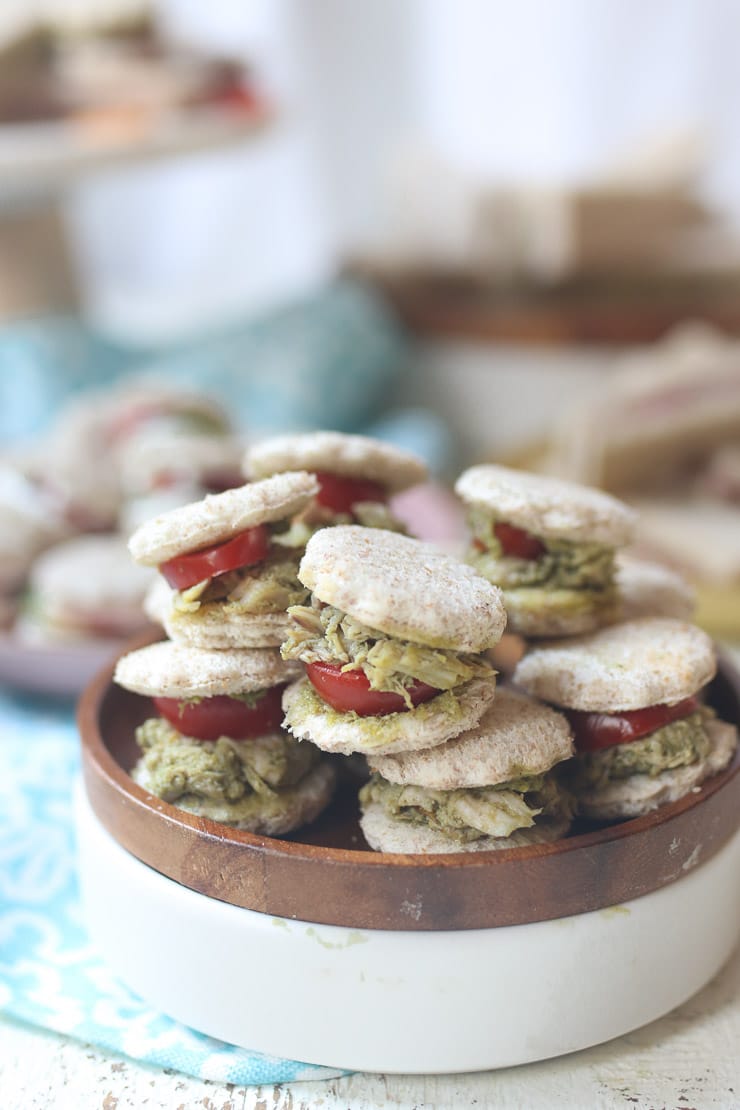 Chicken and pesto finger sandwiche on a wooden plate.