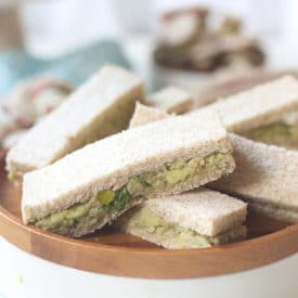 Avocado and salmon finger sandwiches on a wooden plate.
