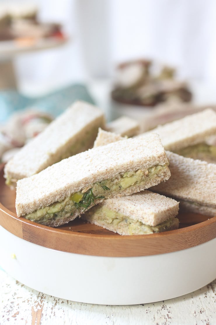 Avocado and salmon finger sandwiche on a wooden plate.