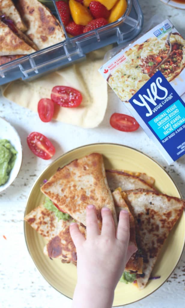 Toddler hand reaching for quesadilla from a yellow plate.