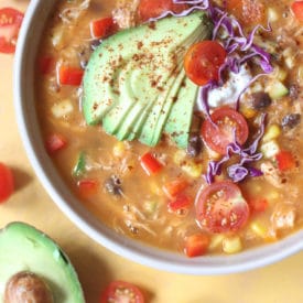 Tortilla soup in a large bowl topped with avocado and cabbage.
