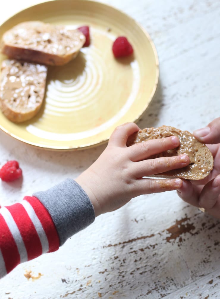 Baby's hand holding a piece of bread with peanut butter. 