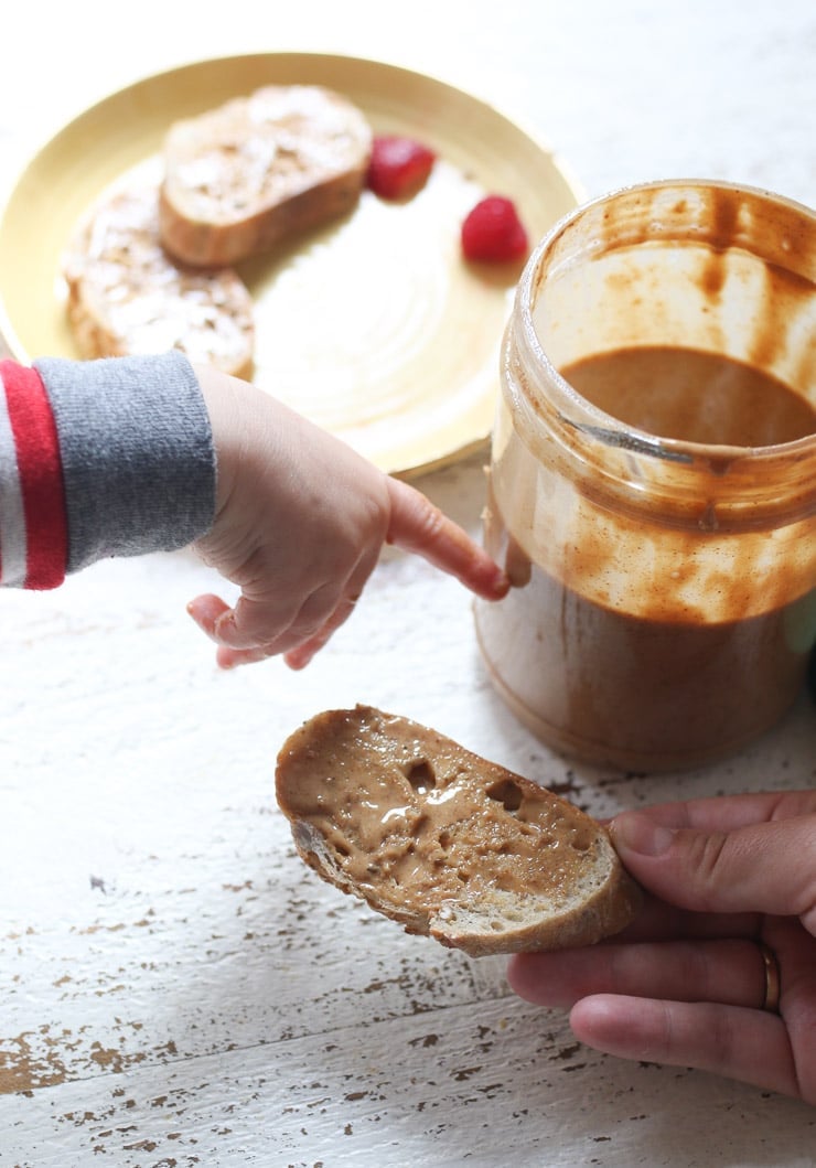 Baby's hand pointing to jar of peanut butter. 