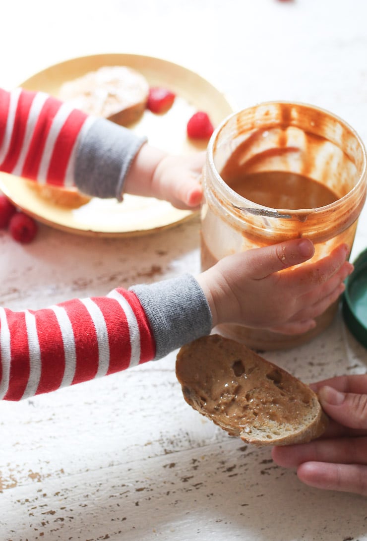 Baby's hand holding a jar of peanut butter. 