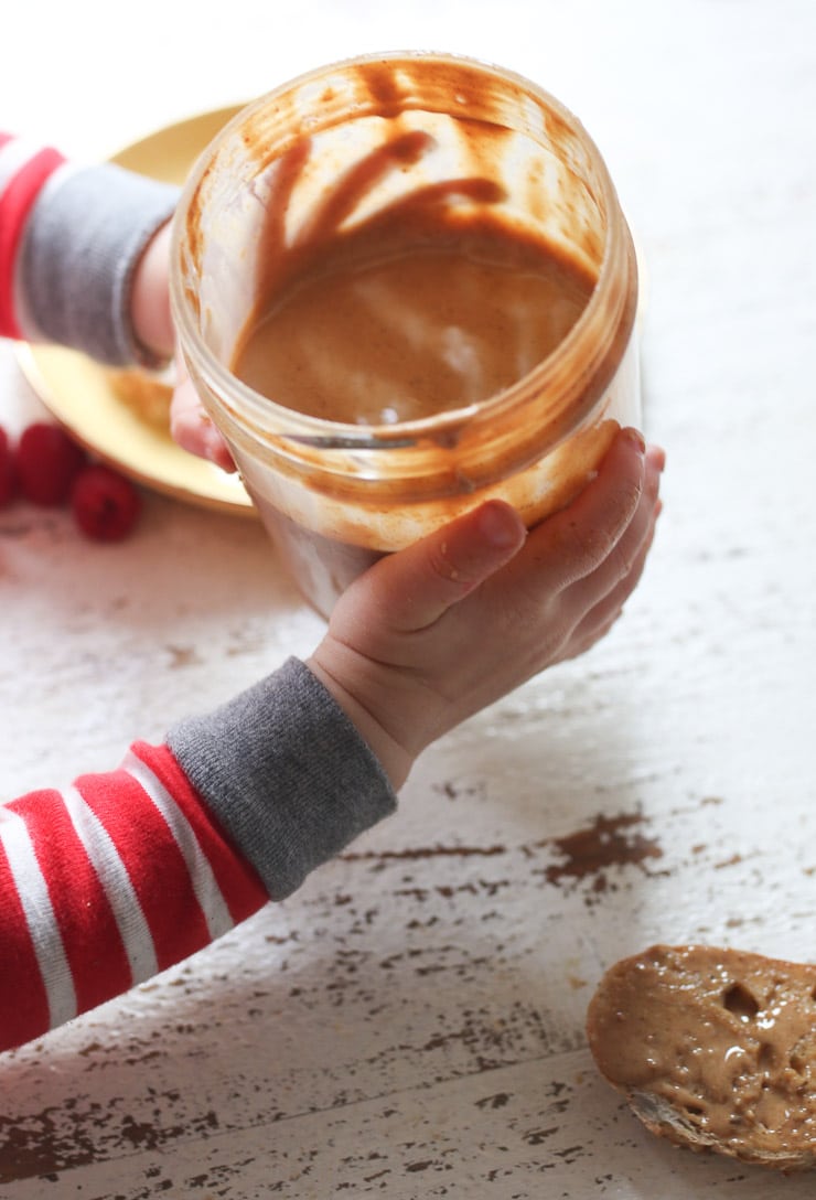 Baby's hand holding jar of peanut butter.