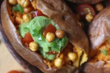 Guacamole and chickpeas stuffed sweet potato served on a wooden plate.