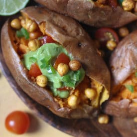 Guacamole and chickpeas stuffed sweet potato served on a wooden plate.