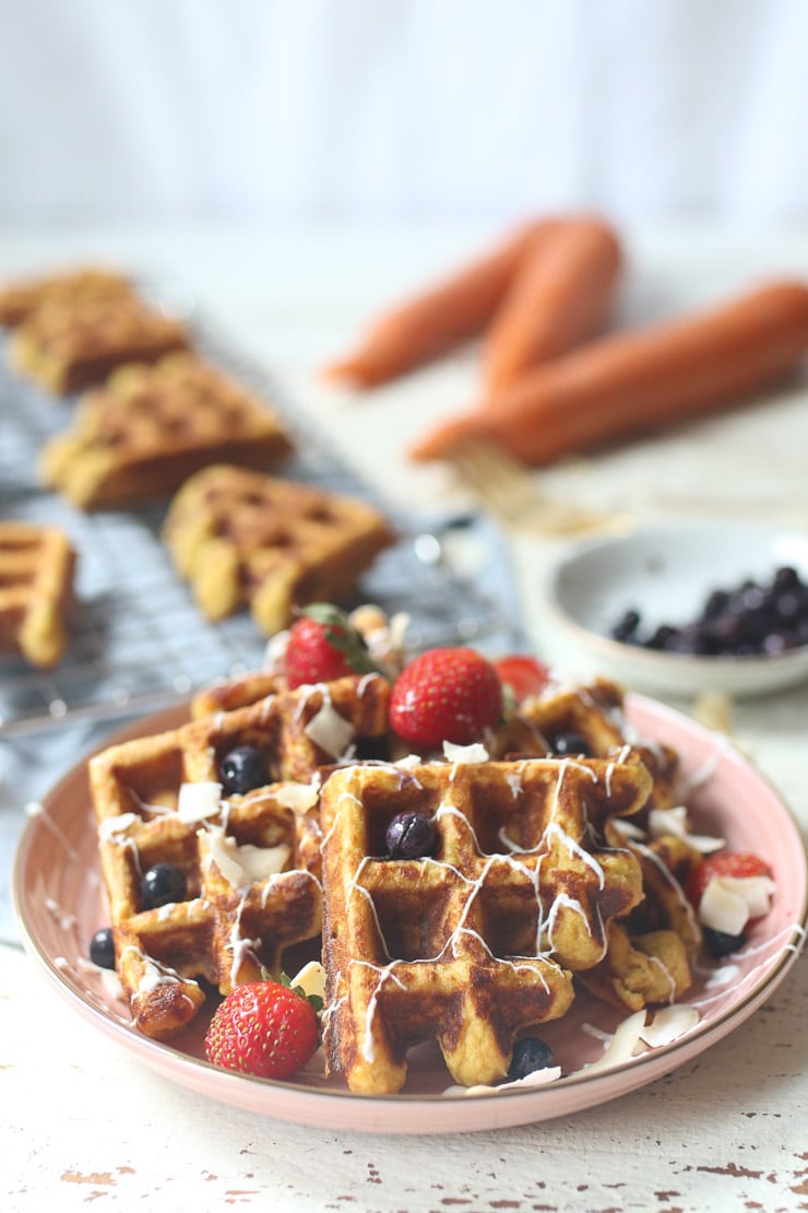 Carrot cake waffles topped with berries on pink plate.