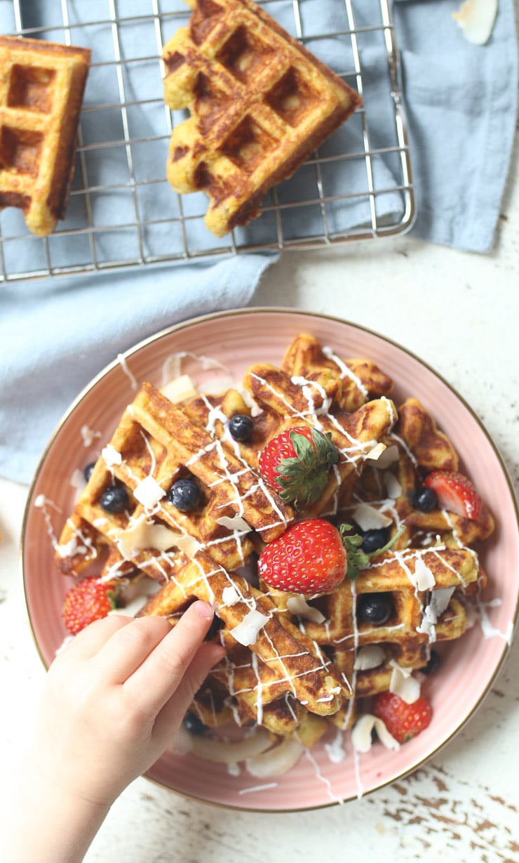 Carrot cake waffle topped with berries on a pink plate.