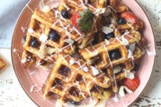 Waffles served on a pink plate topped with berries.